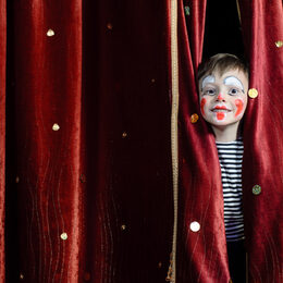 Ein als Clown geschminkter Junge schaut durch einen Vorhang